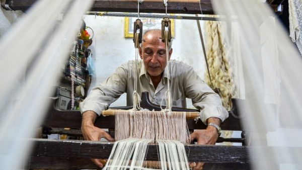 Muhammad Saud, a 65-year-old Syrian silk farmer, handweaves silk threads on a loom at his home workshop in the village of Deir Mama, in west-central Syria on June 22, 2020. MAHER AL MOUNES / AFP