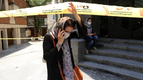 A mask-clad Iranian woman walks past the security cordon at the site of an explosion at the Sina At'har health centre in the upmarket northern neighbourhood of Tajrish in the capital Tehran on July 1, 2020. Iranian police questioned four people as part of investigations into a powerful explosion that killed 19 people at a Tehran clinic the night before, state media reported. ATTA KENARE / AFP