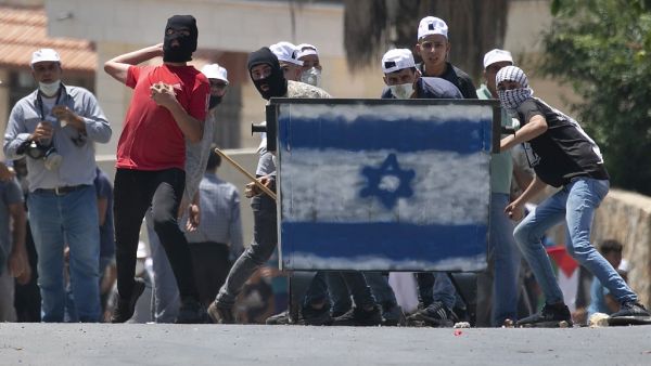 Palestinian protesters, standing behind a shield painted with the colours of the Israeli flag, hurl stones towards Israeli troops (unseen) during a demonstration in the village of Kfar Qaddum in the occupied West Bank against the Jewish state's plans to annex part of the Palestinian territory on July 3, 2020. JAAFAR ASHTIYEH / AFP