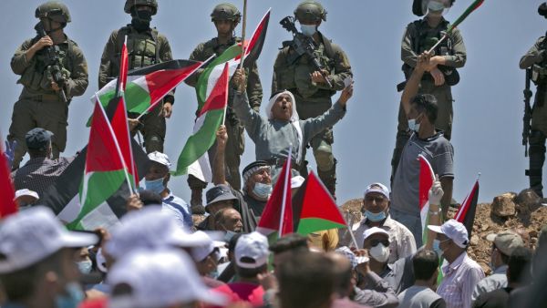 Demonstrators, clad in masks and latex gloves, wave Palestinian flags while Israeli forces stand on guard nearby during a protest against Jewish settlements and Israel's planned annexation of parts of the Israeli-occupied West Bank, in the town of Asira Shamaliya near the West Bank city of Nablus on July 10, 2020. ABBAS MOMANI / AFP