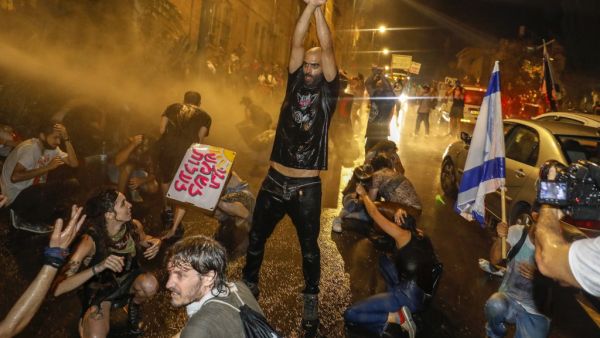 A protestor holds up his fists as Israeli police spray the crowd with water cannon during a rally against Prime Minister Benjamin Netanyahu in Jerusalem, on July 19, 2020 amid the coronavirus pandemic. Israeli police fired water cannons to disperse anti-government protests attended by thousands on Saturday, as public anger mounts over the handling of the coronavirus crisis. Demonstrators gathered outside Prime Minister Benjamin Netanyahu's residence in Jerusalem and at a park in Tel Aviv, voicing frustratio