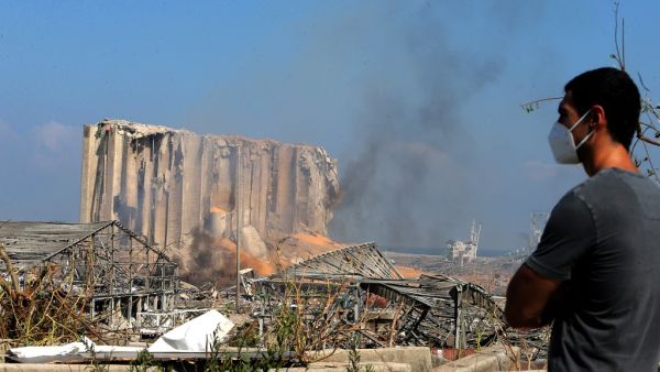 A man wearing a protective mask against the coronavirus stands across the road from the damaged grain silos of Beirut's harbour August 5, 2020, one day after a powerful twin explosion tore through Lebanon's capital, resulting from the ignition of a huge depot of ammonium nitrate at the city's main port. STR / AFP