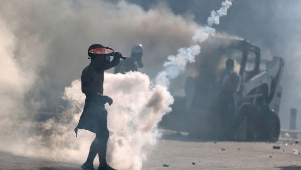 A topless protester wearing a gas mask uses a tennis racket to volley back a tear gas canister during clashes with security forces in downtown Beirut on August 8, 2020, following a demonstration against a political leadership they blame for a monster explosion that killed more than 150 people and disfigured the capital Beirut. PATRICK BAZ / AFP