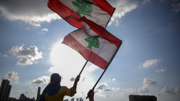 Lebanese women wave the national flag during a commemoration ceremony for the victims of the Beirut port explosion across from the capital's harbour, on August 11, 2020. PATRICK BAZ / AFP