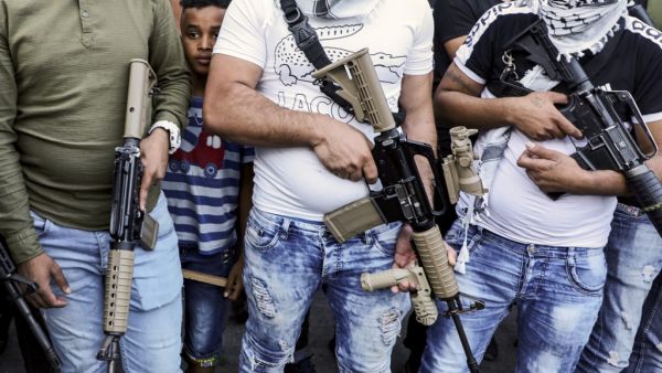 A youth peeks from behind between the shoulders of armed members of the Fatah movement, during a rally against the US-brokered UAE-Israel deal to normalise relations, at the Askar camp for Palestinian refugees east of Nablus in the occupied West Bank, on August 22, 2020. JAAFAR ASHTIYEH / AFP