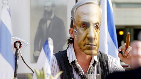 An Israeli comedian, wearing a mask bearing the portrait of Prime Minister Benjamin Netanyahu, smokes a cigar during a fake cabinet meeting to protest the Israeli government's policy and mismanagement of the Covid-19 pandemic in the coastal city of Tel Aviv on September 6, 2020. JACK GUEZ / AFP