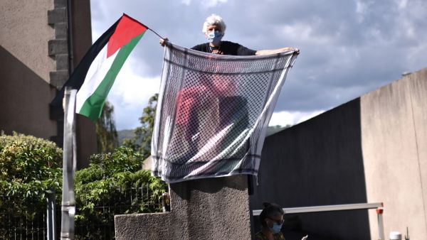 A woman holds a keffiyeh and a Palestinian flag as the pack rides during the 13th stage of the 107th edition of the Tour de France cycling race, 191 km between Chatel-Guyon and Puy Mary, on September 11, 2020. Marco BERTORELLO / AFP