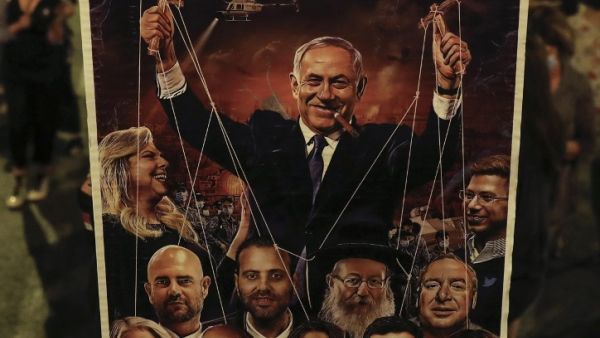 An Israeli protester holds a sign depicting Prime Minister Benjamin Netanyahu as running a string of right-leaning politicians beneath him while his wife Sara laughs, during an anti-government demonstration outside his residence in Jerusalem, on September 20, 2020. Ahmad GHARABLI / AFP
