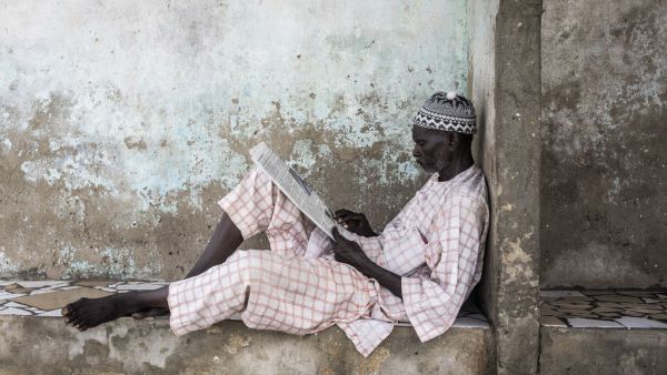 A man reads a newspaper as he waits for the tide to recede in Bargny on September 02, 2020. Fishing villages like Bargny have been fighting the rising seas for decades, hundreds of houses have been lost and families displaced. JOHN WESSELS / AFP