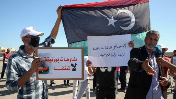 Libyans lift placards during a demonstration to protest upcoming talks between the country's two rival administrations, and demand relying on the constitution to solve the conflict, in front of the headquarters of the United Nations Mission in the city of Janzour, west of the Libyan capital, on October 14, 2020. (AFP/File)