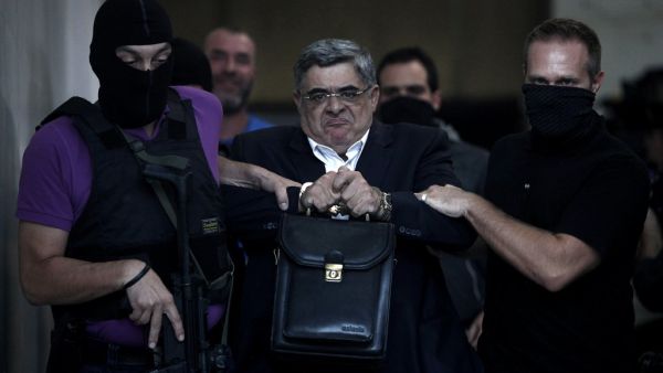  In this file photo taken on September 28, 2013 the leader of ultra-right wing Golden Dawn party Nikos Michaloliakos is escorted by masked police officers to the prosecutor from the police headquarters in Athens. A Greek court on October 14, 2020 handed a 13-year prison sentence to the leader of neo-Nazi group Golden Dawn for running a criminal organisation. As well as Nikos Michaloliakos, the party's founder -- who received an additional one year for illegal possession of a weapon -- the court also sentenc