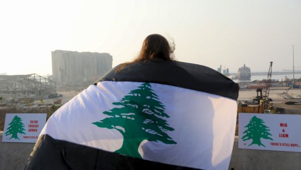 In this file photo taken on September 4, 2020, a woman, draped in a black-striped Lebanese flag, looks at the site of the massive explosion at Beirut's port area, during a demonstration to mark one month since the cataclysmic August 4 explosion that killed 191 people, in the Lebanese capital Beirut. (AFP/File)