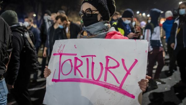 A protestor blocked by riot police guarding the house of Jaroslaw Kaczynski, leader of Poland's ruling Law and Justice party (PIS)holds a poster reading "torture" during a demonstration against a decision by the Constitutional Court on abortion law restriction,in Warsaw on October 23, 2020. Wojtek RADWANSKI / AFP