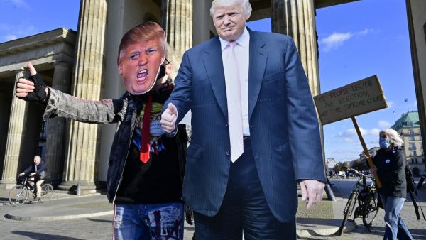 A supporter of US President Donald Trump poses with a cardboard cutout likeness of Trump in front of the Brandenburg Gate as a member of the "Democrats Abroad" organisation (R) walks displaying a placard urging that all ballots be counted, in Berlin on November 4, 2020, as counting continues in the current presidential election. The US election was plunged into chaos early Wednesday November 4, 2020, as President Donald Trump prematurely declared victory and sought Supreme Court intervention to stop vote-co
