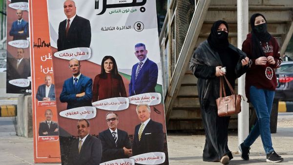 Women, mask-clad due to the COVID-19 coronavirus pandemic, walk past a campaign banner for an electoral list running in the general election scheduled for the following day, along a street in Jordan's capital Amman on November 9, 2020. Voters in coronavirus-battered Jordan go to the polls on November 10 in an election focused on the Arab country's economic crisis which has been heightened by the devastating pandemic. Although there have been some calls on social media to postpone the elections, the governme