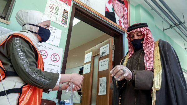 A voter, mask-clad due to the COVID-19 coronavirus pandemic, is assisted by a volunteer to put on a plastic glove before entering a polling station in Jordan's capital Amman on November 10, 2020, during the 2020 general election. AFP