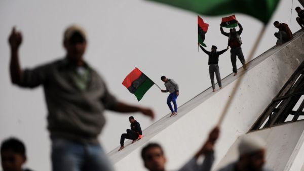 In this file photo taken on March 2, 2011, Libyans wave their old national flag as others celebrate burning copies of the “green book” authored by Libyan ruler Moamer Kadhafi, in the north-central Libyan city of Benghazi. Ten years ago, a wildfire of revolts in the Arab world touched off an unlikely series of events that swelled, then dashed many hopes, and irrevocably changed the region. ROBERTO SCHMIDT / AFP