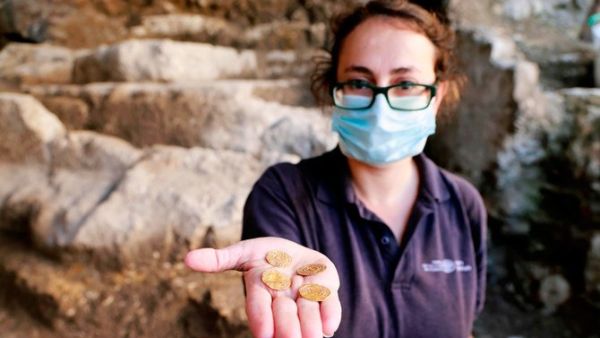 Archaeologist at the Israel Antiquities Authority Evgeniya Rabinovich shows a small pottery jug with four pure gold coins found inside it, at the archaeological rescue excavation site in the Old City of Jerusalem, on November 9, 2020. (AFP)