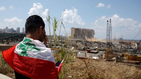 A man draped in a Lebanese flag stands before the ravaged port of Beirut. AFP