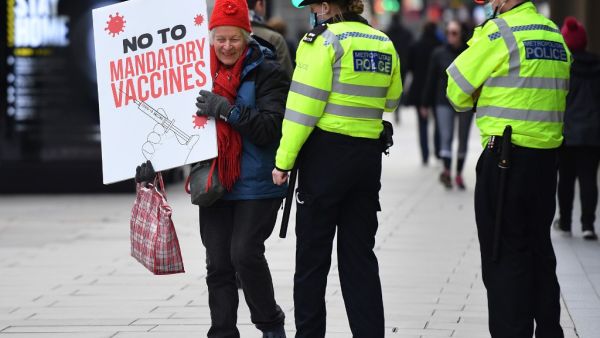 A protestor holding a placard is spoken to by police officers as she attends an anti-vaccine demonstration outside the offices of the Bill and Melinda Gates foundation in central London on November 24, 2020. British Prime Minister Boris Johnson told MPs that thanks to a potential vaccine "the escape route is in sight" from the coronavirus crisis -- while warning that in the immediate future "Christmas cannot be normal". JUSTIN TALLIS / AFP