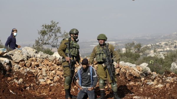 Israeli soldiers detain a Palestinian protester as an Israeli settler hurls rocks at Palestinians during a demonstration against the expansion of settlements in the occupied-West Bank town of Salfit, near the Israeli settlement of Ariel, on November 30, 2020. JAAFAR ASHTIYEH / AFP Israeli soldiers detain a Palestinian protester as an Israeli settler hurls rocks at Palestinians during a demonstration against the expansion of settlements in the occupied-West Bank town of Salfit, near the Israeli settlement of Ariel, on November 30, 2020. JAAFAR ASHTIYEH / AFP