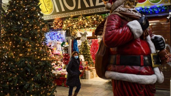 A woman wearing a protective face mask walks past a Santa Claus outside a shop selling Christmas decoration, in Athens, on December 7, 2020. ANGELOS TZORTZINIS / AFP