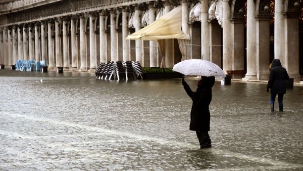 A person takes photos while standing on a flooded St. Mark's Square on December 8, 2020 in Venice following a high tide "Alta Acqua" event following heavy rains and strong winds, and the mobile gates of the MOSE Experimental Electromechanical Module that protects the city of Venice from floods, were not lifted ANDREA PATTARO / AFP