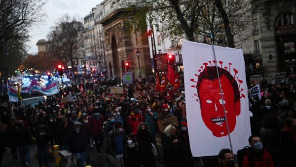 A protester holds a sign showing the French President Emmanuel Macron as a virus during a demonstration in Paris on december 12, 2020, against the 'global security' draft law. It is the third weekend of demonstrations in France during protests against a security bill currently going through French parliament, that would restrict publication of pictures showing the faces of police. Christophe ARCHAMBAULT / AFP