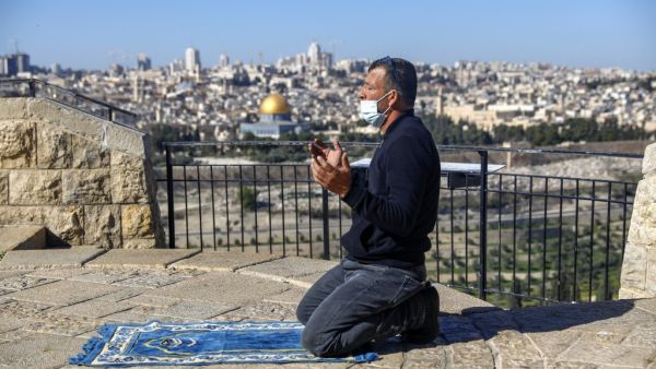 A mask-clad Palestinian, unable to reach the Al-Aqsa mosque compound amidst strengthened restriction due to the coronavirus, perform Friday prayers at the Mount of Olives overlooking the compound in the Old City of Jerusalem on January 8, 2021. AHMAD GHARABLI / AFP