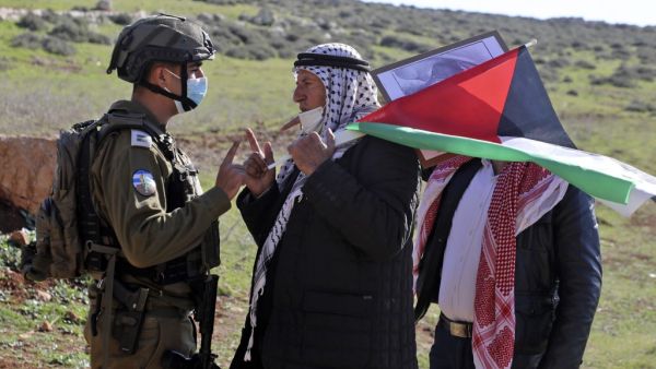 A Palestinian protester carrying the national flag confronts Israeli security forces during a demonstration against the expansion of settlements near the village of Beit Dajan, east of Nablus, in the occupied West Bank, on January 8, 2021. JAAFAR ASHTIYEH / AFP