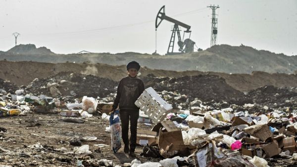 A Syrian child sifts through a garbage dump near an oil field in the countryside of Malikiya in northeast Syria, on January 12, 2021. On the dry plains outside the city of Al-Malikiyah, a dozen people wrapped up against the cold rip open the black plastic bags, in a desperate search for something to sell, repurpose or even eat. Across the road, an oil pump swings back and forth in this resource-rich region controlled by US-backed Kurdish forces.  Delil SOULEIMAN / AFP