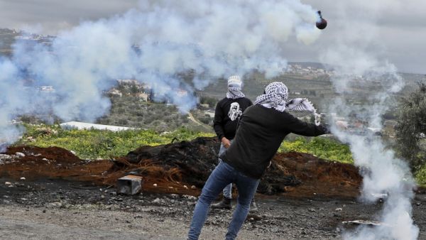 Palestinian protesters use slingshots to hurl rocks amid billowing tear gas during clashes with Israeli troops in the village of Kfar Qaddum near the Jewish settlement of Qadumim (Kedumim) in the occupied West Bank, following a demonstration against the expropriation of land by Israel, on January 15, 2021. JAAFAR ASHTIYEH / AFP