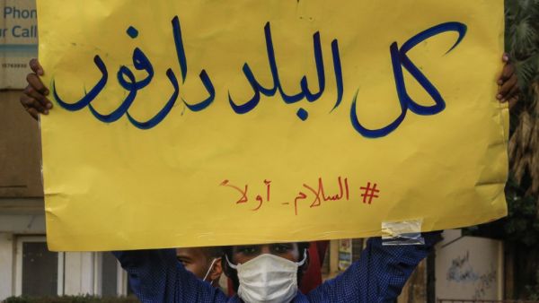 In this file photo taken on July 4, 2020, A mask-clad demonstrator (due to the COVID-19 coronavirus pandemic) stands with a sign reading in Arabic "all of the country is Darfur, #PeaceFirst", during a protest outside the Sudanese Professionals Association in the Garden City district of Sudan's capital Khartoum, in solidarity with the people of the Nertiti region of Central Darfur province in the country's southwest. ASHRAF SHAZLY / AFP