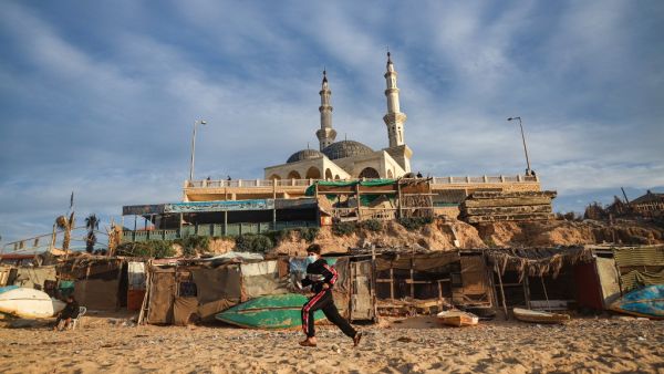 A Palestinian boy wearing a mask for protection against the COVID-19 coronavirus pandemic runs along a beach beneath a mosque in Gaza City on January 27, 2021. MOHAMMED ABED / AFP