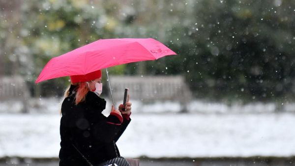 A pedestrian wearing a face mask or covering due to the COVID-19 pandemic, shelters from the snow beneath an umbrella in Green Park in central London on February 9, 2021. Cold weather swept across northern Europe bring snow and ice. JUSTIN TALLIS / AFP