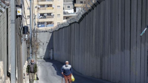 Palestinian men walk by Israel's controversial barrier separating the West Bank city of Abu Dis (background) and East Jerusalem (foreground), on February 16, 2021. AHMAD GHARABLI / AFP