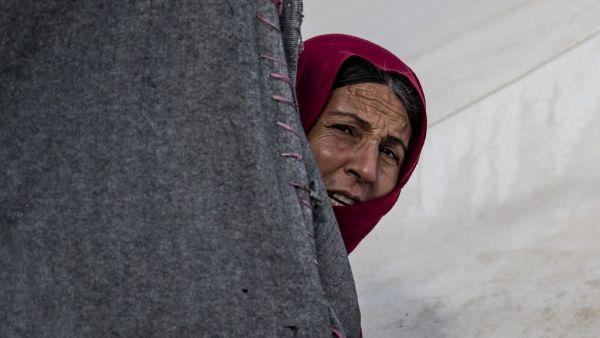 A woman looks on from behind a tent at the Kurdish-run al-Hol camp which holds suspected relatives of Islamic State (IS) group fighters, in the northeastern Syrian Hasakeh governorate, on February 17, 2021. Delil SOULEIMAN / AFP