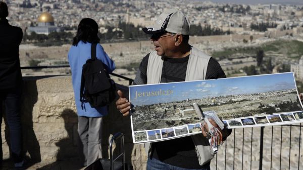 A vendor sells souvenir postcards to tourists watching Jerusalem's Old City from the panoramic view of the Mount of Olives, January 2019 (AFP)
