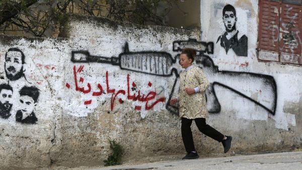 A Palestinian woman walks past a pro-Hamas mural 