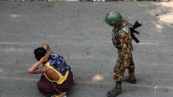 A soldier stands next to a detained man 