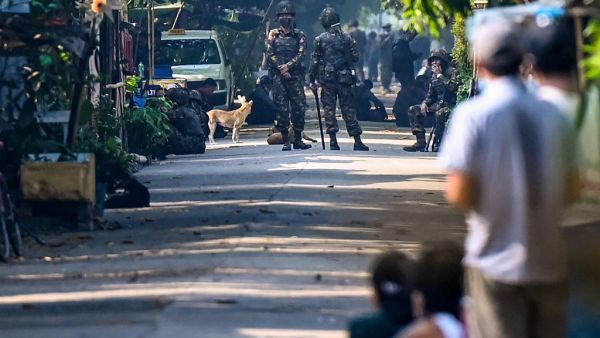 Residents look on as soldiers block a road