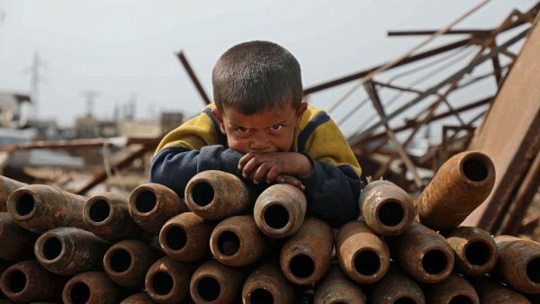 A Syrian child poses atop a stack of neutralised shells at a metal scrapyard