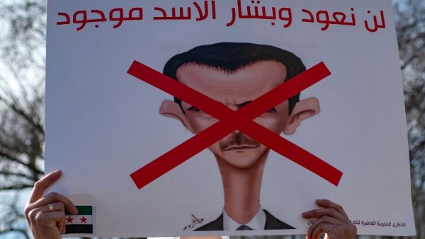 A Syrian woman holds up a banner that reads, 'We will not return as long as (Syrian President) Assad is present'
