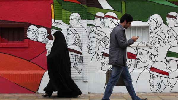 People walk in the Imam Khomeini Street with background street art