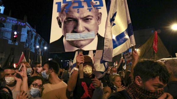 Israeli protesters hold a poster of PM Netanyahu gagged by a surgical protection mask 