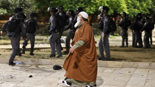 A Palestinian man walks amid the clashes between Israeli police and Palestinian protesters at al-Aqsa mosque compound in Jerusalem