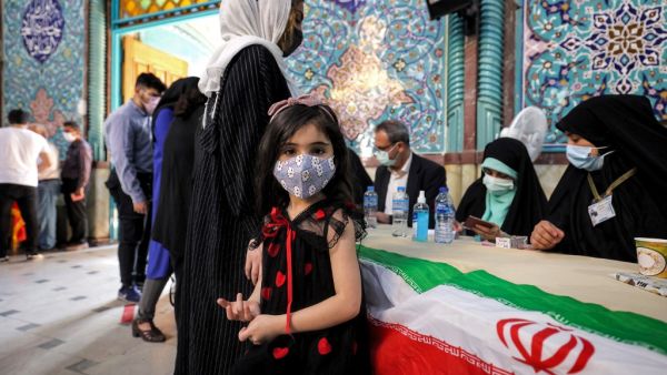 A girl looks on as a woman registers to vote at a polling station polling station in Iran's capital Tehran on June 18, 2021, during the 2021 presidential election. Iranians voted on June 18 in a presidential election in which ultraconservative cleric Ebrahim Raisi is seen as all but certain to coast to victory after all serious rivals were barred from running