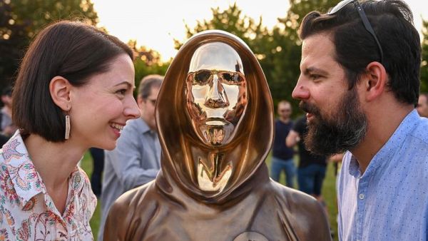 Hungarian sculptors and creators Reka Gergely (L) and Tamas Gilly (R) pose next to the statue of Satoshi Nakamoto