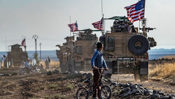 A Syrian boy on his bicycle looks at a convoy of US armoured vehicles patrolling fields near the northeastern town of Qahtaniyah at the border with Turkey, on October 31, 2019. AFP / Delil SOULEIMAN Syria’s military base in Dayr al-Zawrhit hit by a series of large explosions