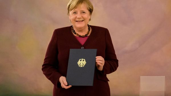 German Chancellor Angela Merkel poses with her dismissal certificate during an official dismissal ceremony presided by the German President on October 26, 2021 at the Presidential Bellevue Palace in Berlin. (Photo by JENS SCHLUETER / AFP) German Chancellor Angela Merkel